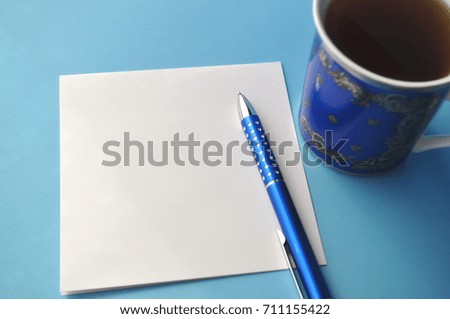 Dark blue fine porcelain china tea or coffee cup with a blank note card, blue, teal and aqua pencils on white and blue background