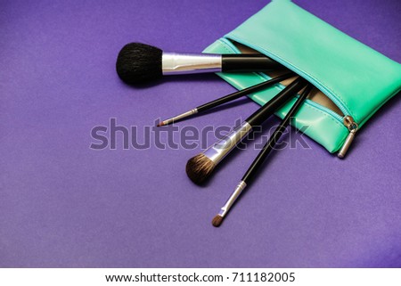 Make-up brushes in green mint cosmetic bag on a bright purple background. Empty place to copy paste text.