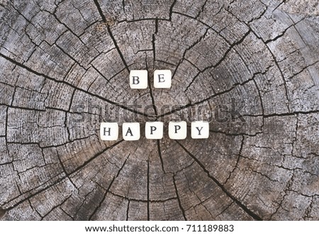 Words be happy of wooden alphabet beads on a tree stump surface in the forest.