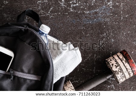 Fitness accessories on the dark floor in the gym. Dumbbell, black sport bag, smart phone, towels, water bottle. Cares about a body. Sport concept. Top view. 