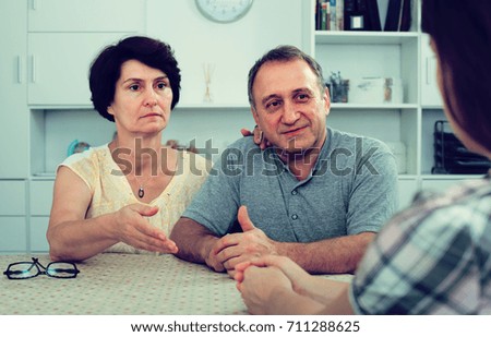 Senior parents attentively listening and talking to woman indoors  
