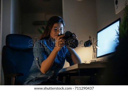 Young photographer looking at her camera and working at night.