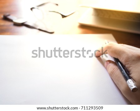 Businesses happen everywhere, just have inspiration. The picture of white laptop, hand, pencil and glasses on wooden table near the window at home office with sunshine effect. selective focus