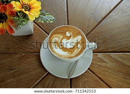 Top view of coffee latte art style with swan Lake picture in white ceramic cup on wooden table with vivid yellow flower background.