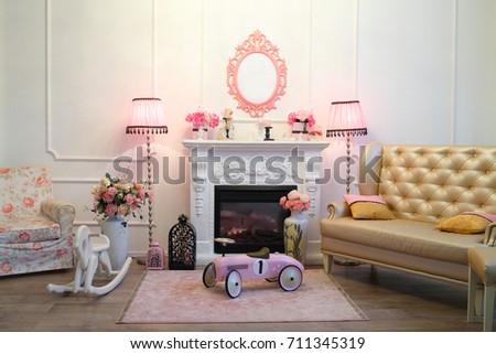 The interior of the living room in a romantic style with a fireplace, two pink floor lamps, a sofa and a childrens retro car and wooden horse