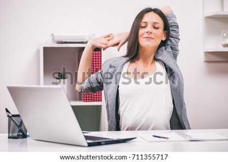 Young businesswoman is relaxing in her office. She is stretching her body.  Royalty-Free Stock Photo #711355717