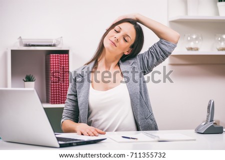 Young businesswoman is relaxing in her office. She is stretching her body.  Royalty-Free Stock Photo #711355732