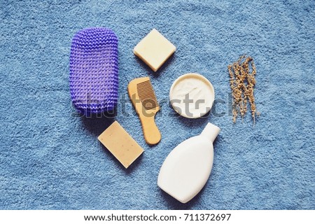 Purple sponge, natural organic handmade soap bars, body cream, shampoo bottle and wormwood herbs on a blue cotton towel. Bathroom items flat lay, top view photo. Bath products, spa cosmetics