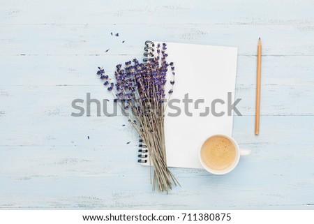 Morning cup of coffee, clean notebook and lavender flower on blue background top view. Woman working desk. Cozy breakfast. Flat lay style.