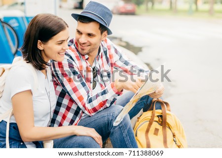 Portrait of happy male and female friends, having trip, resting on park bench, looking happily into map, choosing place where to go. Young tourists having vacation using city map. Relaxation concept