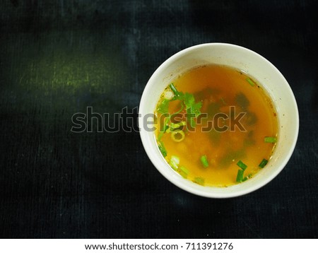 Top view of Thai local traditional clear soy sauce pork stock soup with coriander parsley  vegetable, grounded white pepper and spring onion in small ceramic cup, on black table