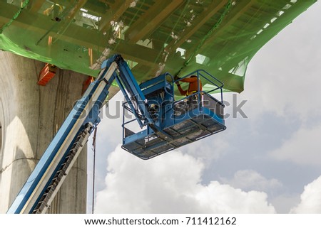 Workers in scissor lift platform on a construction site. / Worker on the lift machine. / Construction workers standing in the crane bucket while working at high level in the construction site Royalty-Free Stock Photo #711412162