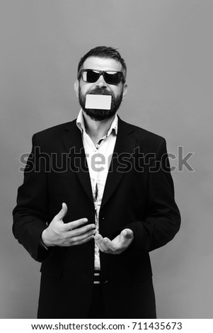 Guy with funny face and sunglasses isolated on green background. Businessman and empty card with copy space. Business and people at work concept. Man with beard holds green business card in teeth