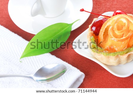 Closeup of cupcake with jelly and fruits on a white plate and a cup of coffee on a brown background