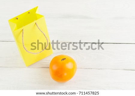 Single yellow ripe tomato and yellow paper bag on old white rustic wooden planks