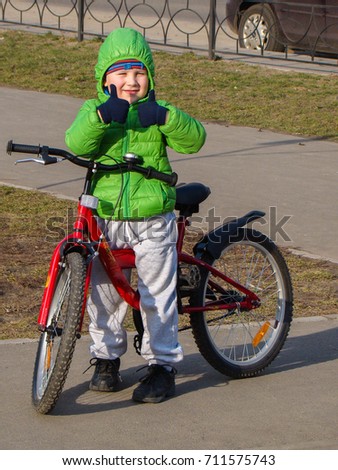 A child in a bright jacket learns to ride a bicycle and shows thumbs up