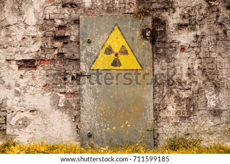 Radioactive (ionizing radiation) danger symbol painted on the old massive rusted iron door of an abandoned structure with grunge walls and overall derelict atmosphere. Royalty-Free Stock Photo #711599185