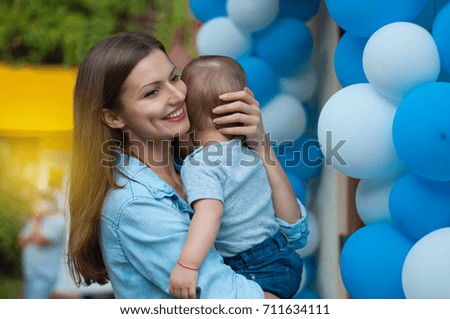 Portrait of young beautiful mom hugging and caressing her baby boy on balloons background
