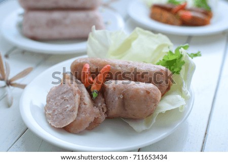 grilled sour pork sausage and sliced  on white  plate and white wood table, This Thai food is called " naem moo ".