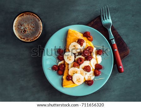 Omelette with bananas and red berries on a blue plate. Dark food photography. Vintage edited image filter 
