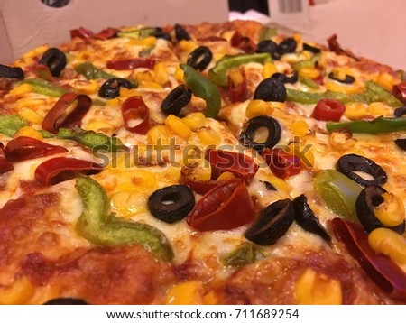 Delicious veg pizza with cheese, olives, paprika, corn, capsicum toppings. Close up shot.