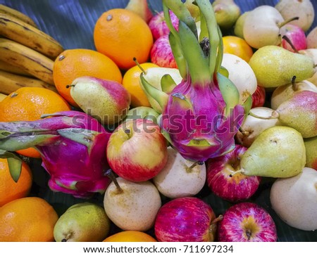 image of various colourful fruits on banana leaf. only focus around purple dragon fruit on right. gradient blur background.