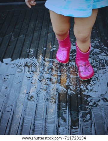 Baby with pink boots step on a water puddle after raining. Happy baby playing a puddle