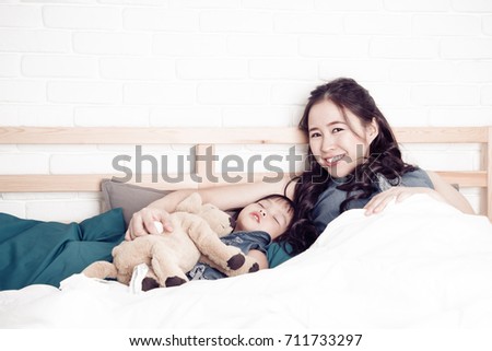 Proud mother watching to sleep on the bed to her daughter
with Dog doll.