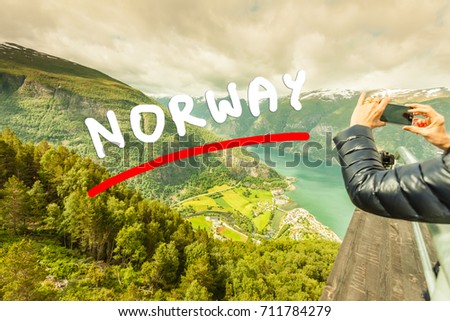 Tourism vacation and travel. Woman tourist taking photo with smartphone, enjoying Aurland fjord view from Stegastein viewpoint, Norway Scandinavia.