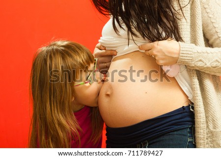 Family, pregnancy concept. Toddler girl kissing her mother pregnant belly.