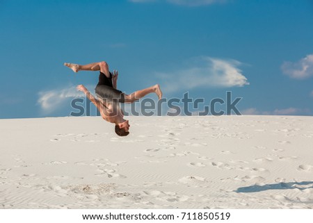 Portrait of young parkour man doing flip or somersault on the sand. Royalty-Free Stock Photo #711850519