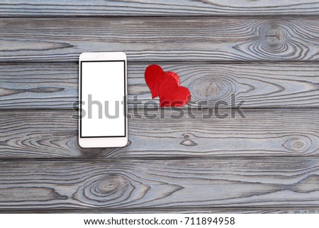 Smartphone with a white screen, hearts on a wooden background.