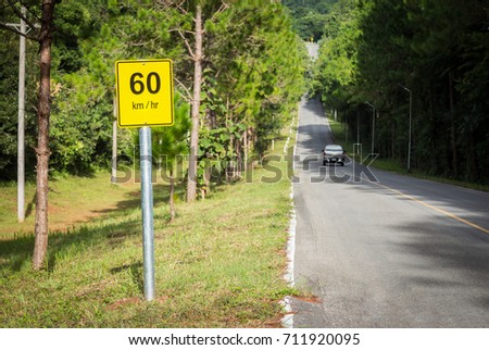 60 Km per hour traffic sign post on mountain road with moving car with pine forest view 