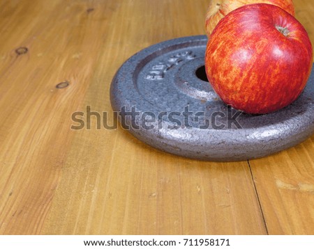 Weight plate and red apple on brown wood floor. Exercise and eating healthy food concept. Good health. Benefit of health food and exercise.