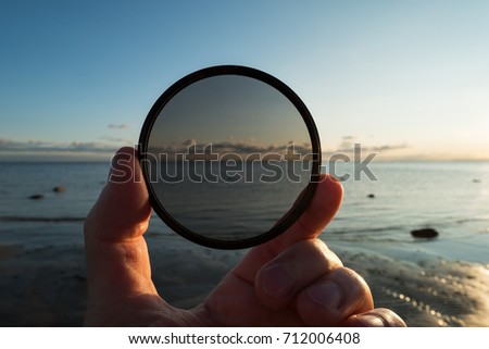 Man holding gradient neutral density ND filter on background of sea and sky