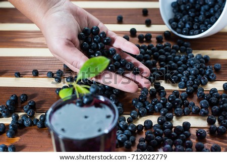 Female hand with aronia and bowl full of aronia spilled on wooden table with glass of aronia juice