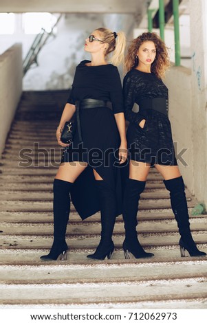 Two Stylish fashionable girl with blonde long hair,  stylish black dress posing. Fashion trendy woman concept