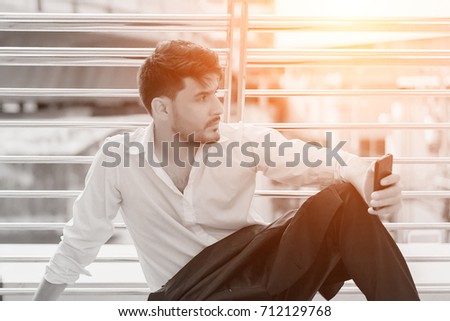 Image processing color tone of Handsome businessman sitting outdoors and holding smartphone. concept of relax, feeling, technology and attractive.