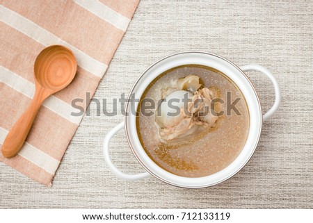 Bowl of pork bone soup with herbs on gray table mat with wooden spoon