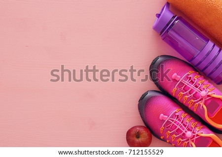 fitness concept with bottle of water, towel and woman pink sport footwear over colorful background.