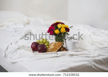 Breakfast for two in bed with croissants, fruits and flowers on a tray. Morning
