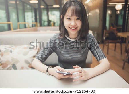 beautiful aisan woman is using a smart phone with smile in office, soft focused image