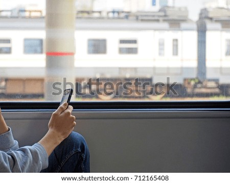 Young teenage boy travelling to school or institute by suburban train sitting in wagon coach sending text message to somebody using his smart mobile phone. Copy space for your text or logo