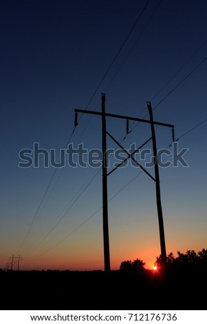 A shot of a power line with wires with the silhouettes of the poles at golden hour with a blue sky just before sunset. Shot north of Hutchinson Kansas.