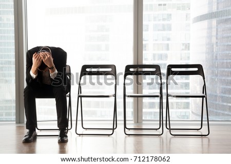 Stressed upset businessman sitting on chair, in waiting room, received bad news. Devastated CEO fired by his boss because of failed business project. Job candidate received refusal from HR department. Royalty-Free Stock Photo #712178062