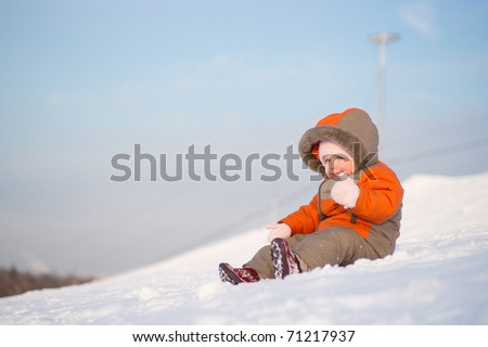 Adorable baby sit on mountain side on sunset and try to slide down