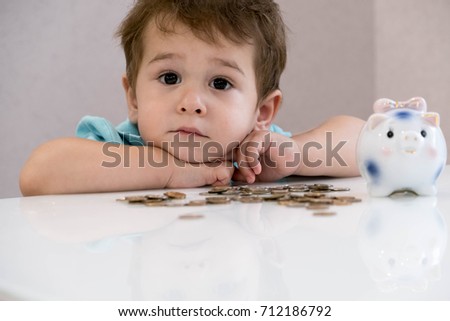 Blurred baby boy putting some coins into other ones, focus on the coins, indoor financial concept. 