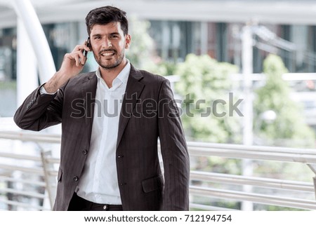 Mobile office concept.  Handsome successful white business man or sale man talking on his cell phone with financial building in background. Taken outdoor, apply urban looks effect.