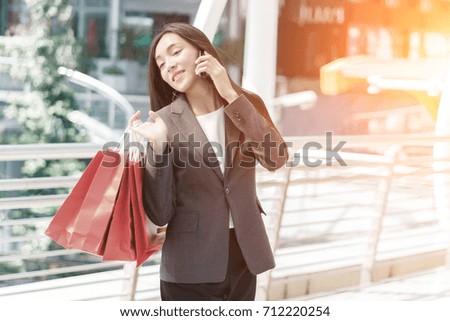 Beautiful shopper woman hand shopping with a smartphone and carrying red bag. concept of woker shopping and business online.