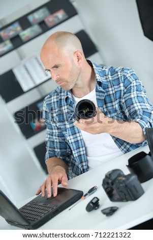 man holding camera lens and looking at laptop